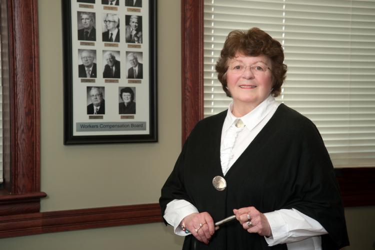 Nancy Guptill as chair of the Worker's Compensation Board stands in front of a composite of former chairpersons